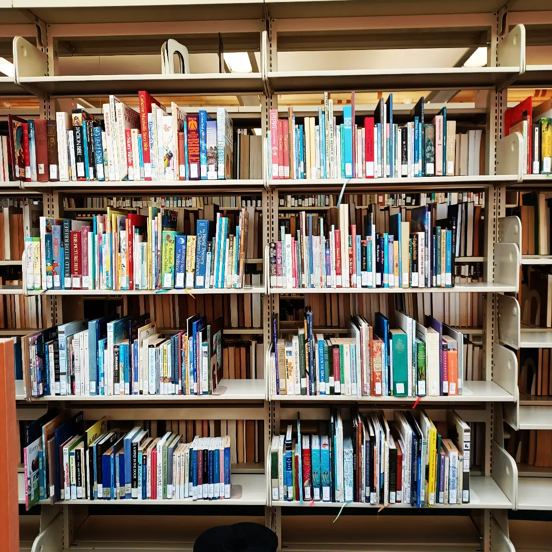 A library shelf filled with books of different shapes, sizes, and colors. 